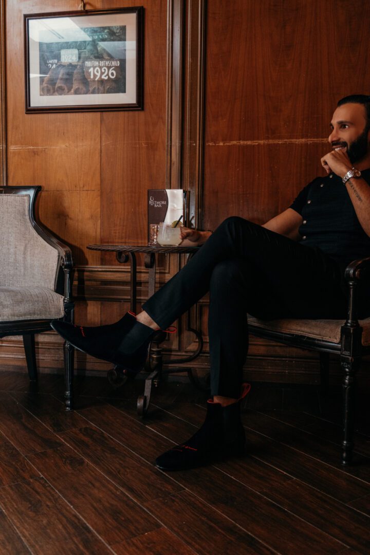 A man in black colored dress and loafers sitting and smiling