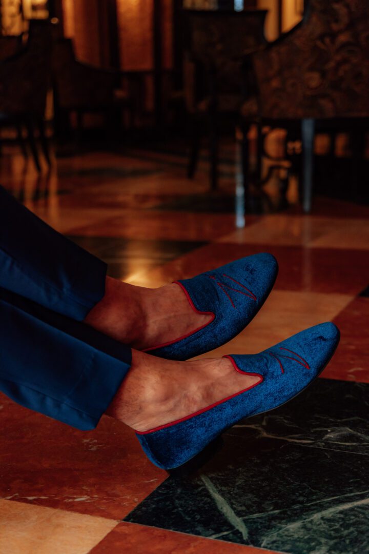 A picture of blue and red color velvet loafers with logo